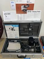 Sony DXC-1610 color video camera and BP-60 battery pack inside open professional carrying case, with original manuals displayed behind.