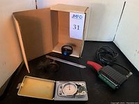 Composition showing the spotmaster tape timer case open, magnetometer, demagnetizer, ruler, and strap on black surface.