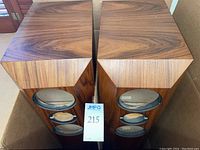 Top view of two wooden tower speaker boxes displaying the bookmatched walnut veneer pattern and three speaker openings on each front panel.