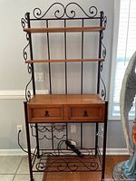 Full view of bakers rack showing wood shelves, drawers, and metal frame with scrollwork.