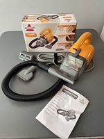 Bissell CleanView Deluxe corded hand vacuum with hose, brush attachment, user manual, and original box arranged on tabletop.