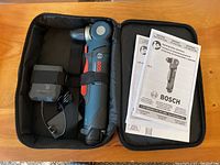 Open carrying case showing Bosch PS11 cordless right angle drill, charger, and instruction manuals inside.