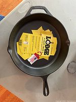 Top view photo of the 12 inch Lodge cast iron skillet showing the skillet with original yellow tags inside, placed on a gray surface.