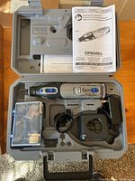 Dremel 8220 cordless rotary tool and accessories organized inside a molded plastic carrying case, showing the rotary tool, battery charger, and accessory box.