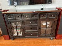 Front view showing the dark wooden cabinet with five small drawers on top, three center drawers, and two glass-front storage compartments filled with items not included in the sale.