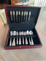 Overview of flatware pieces arranged inside an open wooden presentation box with a velvet lining.