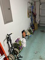 Overview photo of gardening supplies and tools lined along a garage wall, including bags of soil and fertilizer, and manual aerator/seeder.