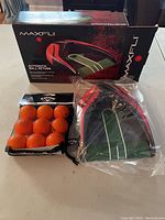 Photo of Maxfli automatic ball return box with the device in plastic wrap and a pack of Callaway orange golf balls