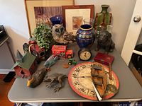 Full view of the assortment on the table showing all the major items including sculptures, framed art, toys, and decorative pieces.