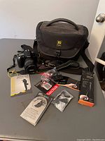 Photo of Nikon DSLR camera, Ruggard shoulder bag, memory card, tripod, and accessories arranged on table.