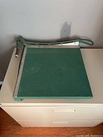 Full view of the vintage paper cutter showing green grid cutting area and metal handle.