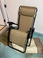 Outdoor folding recliner chair shown unfolded from side angle, highlighting the frame, fabric seating, armrests, and headrest pillow.