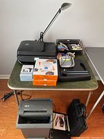 Overview of office items on table including HP printer, desk lamp, stapler, paper packs, wire organizer, and computer bag.