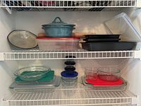 Shelf with various glass pie plates, casserole dishes, small glass bowls, plastic containers with lids, black loaf pans, and a teal ceramic casserole pot with lid.