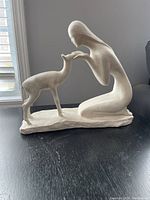 Side view of sculpture showing woman reaching out to deer on black surface near window providing natural light.