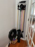 Resistance bands hung on a wall rack with handles and ankle straps, inflatable balance disc and yoga mat on the floor, fitness accessories in a box.