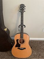 Front view of left-handed Taylor acoustic guitar on stand beside open hardshell case