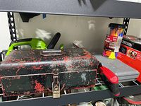 Image showing vintage black and red toolbox, green trimmer, rubber mallet handle, Dremel silver toolbox, and other stored tools on metal shelf