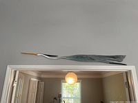 Full view of the wooden bird mounted on a wall above a door frame, showing its elongated shape and the painted details.