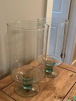 Pair of transparent glass candle holders on wooden surface, showing cylindrical bodies with pedestal base.