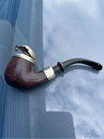 Antique wooden smoking pipe with rusted metal cover and curved black stem on reflective surface