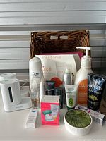 Showcases assorted bathroom and personal care items, including boxed Clarisonic Pedi Sonic Foot Buffer, various lotions, creams, gels, bottles, and tubes, plus a brown wicker basket.