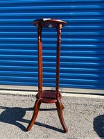 Full view of the tall wooden plant stand showing round top and curved legs.