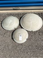 Three round glass ceiling light fixtures placed outdoors on asphalt. Largest fixture features a leaf pattern with small metal clips. Medium fixture has a swirl pattern in white frosted glass. Smallest fixture is a similar style with a smaller swirl pattern.