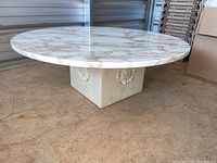 Side angle image of round marble top coffee table with decorative square wooden base decorated with rosette carvings.