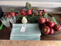 Top view of the entire lot showing metal candle holder with faux pomegranates and berries, pear-shaped candle, teal placemats, metal bowl with faux pomegranates, glass votives, and drinking glasses.