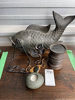 All four items displayed on a wooden table: resin fish sculpture on stand, metal rose, wooden candle holder, stone candle holder with tea light.