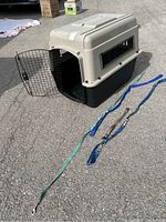 Medium size pet crate with metal door open, three nylon leashes and one dog collar laid out on pavement