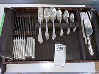 Full flatware set arranged in storage case showing knives, forks, spoons, and serving pieces in compartments