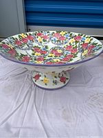 Side view showing the colorful floral pattern with pink roses, yellow, blue, and purple flowers and green leaves on the pedestal bowl.