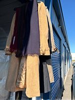 Side view of four men's coats hanging on rack along with scarves in dark red, navy blue, and gray colors showing fabric textures and colors.