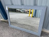 Framed beveled mirror leaning against a metal wall outdoors showing full size and frame details.