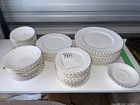 Overall view of multiple stacks of white porcelain dinnerware with gold-trimmed scalloped edges