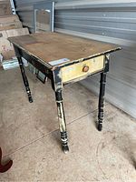 Side angled view of the rustic hall table showing turned legs, drawer, and distressed black and cream paint finish.
