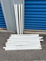 Several white solid wood spindles stacked horizontally with a few standing vertically against a wall, showing overall quantity and condition.