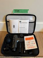 Taotronics massage gun, multiple removable heads, documents and charging cable inside a zippered black carrying case on the floor.