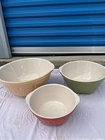 Three ceramic mixing bowls of different sizes and colors laid on a white cloth.