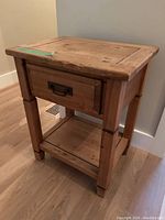 Angle view showing the front left side, drawer with metal handle, and lower shelf of the wooden side table.