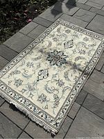 Full view of small Persian Naeen rug laid flat showing overall cream base and floral motifs with fringe ends.