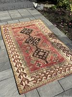 Full view of vintage Shiraz wool rug on outdoor stone floor showing the three medallion pattern and pink salmon color with patterned borders.