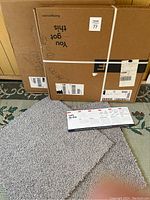 Two cardboard boxes labeled as Shaw Floors with carpet squares placed in front on a patterned carpet floor. The carpet squares are light gray and measure 12x12 inches each, matching seller description.