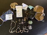 Full lot overview showing jewelry items scattered and multiple pouches and boxes arranged on black surface.