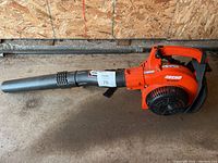 Orange Echo PB-250LN gas leaf blower resting on a concrete floor against a wall.