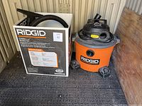 Entire RIDGID shop vac unit shown with original box and main vacuum unit side-by-side on floor.