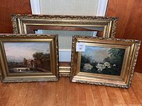 Group shot of two framed oil paintings and one empty frame stacked behind