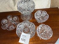 Overview of the five cut crystal items including pedestal candy bowl, small candy dish, and three plates arranged on wood surface.